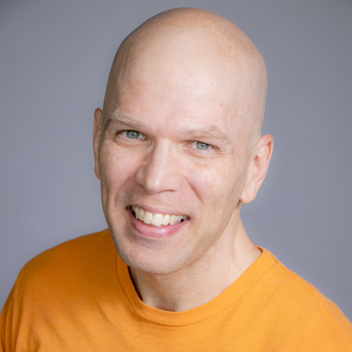 Headshot of Dale Roberts, a bald man wearing an orange shirt, smiling warmly against a neutral gray background.